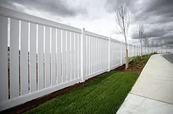 A white fence with grass and trees in the background